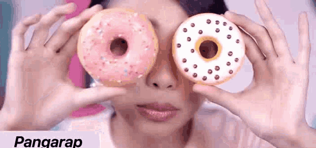 a woman is covering her eyes with two donuts .
