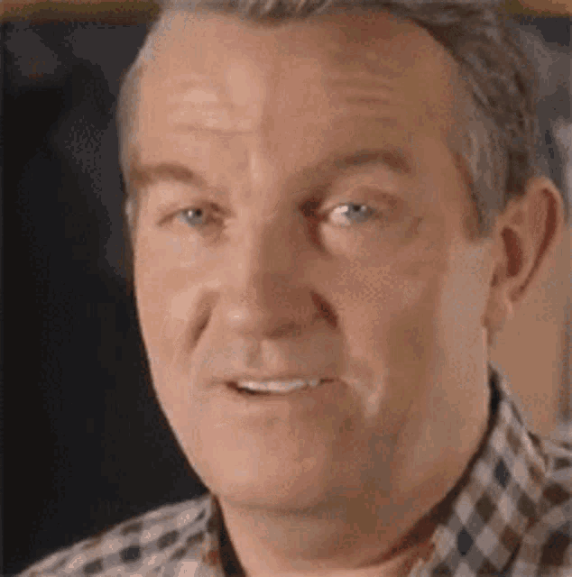 a man wearing a plaid shirt is smiling and looking at the camera .
