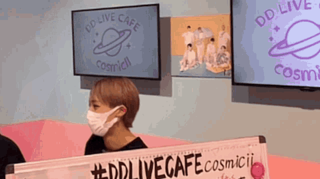a person wearing a mask behind a sign that says #ddlivecafe
