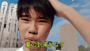 a man scratches his head in front of a fence with chinese writing