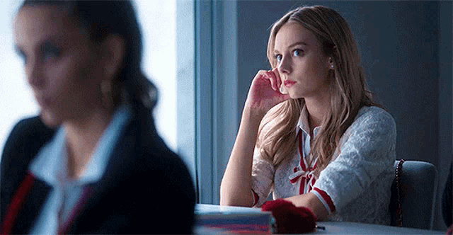 a woman is sitting at a table in front of a window with her hand on her face .