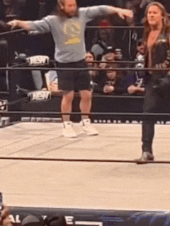 a man is standing in a wrestling ring with his arms outstretched and a woman is standing behind him .