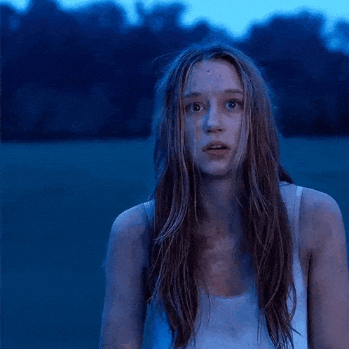 a woman in a white tank top is standing in a field with a blue sky in the background .