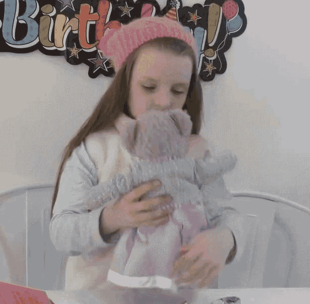 a little girl wearing a pink hat is hugging a stuffed animal