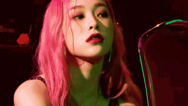 a woman with pink hair is sitting in a chair with a green light behind her