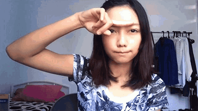 a woman covering her face with her hand in front of a clothes rack