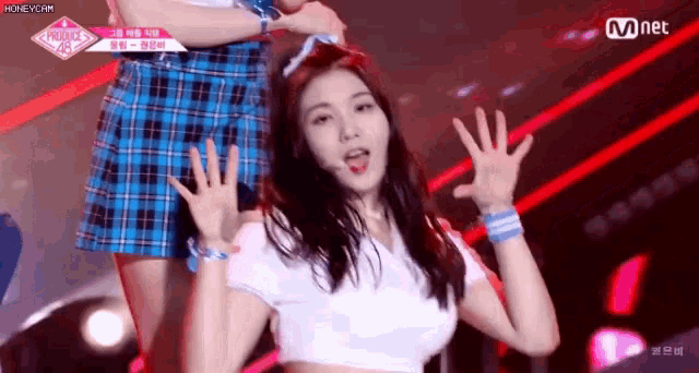 a woman in a white crop top and plaid skirt is dancing on a stage with her hands in the air .