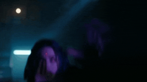 a woman is standing in a dark room with a purple light behind her .