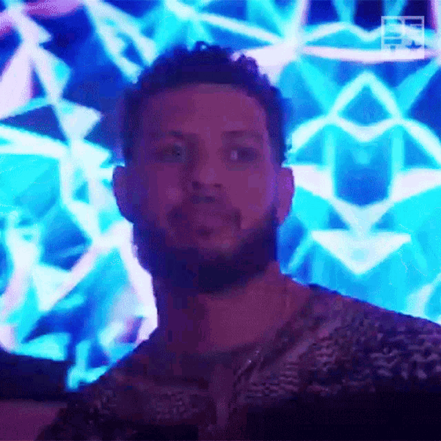 a man with a beard is standing in front of a blue and purple light .