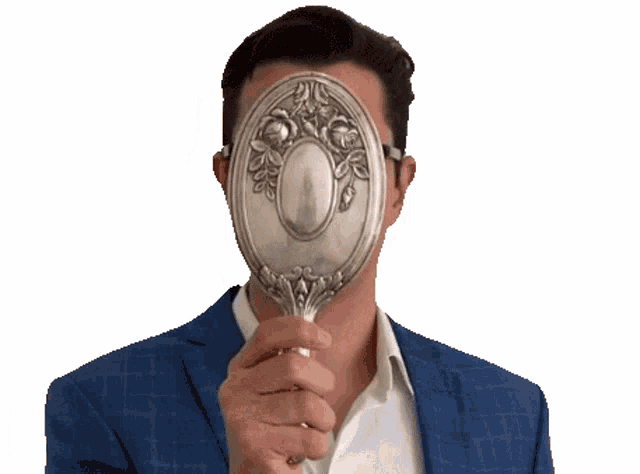 a man in a blue suit and white shirt is holding a silver mirror in front of his face