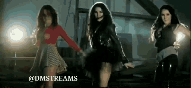 a group of three women are dancing in a dark room with a light behind them .