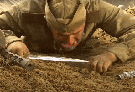 a man in a military uniform is laying in the dirt with a gun