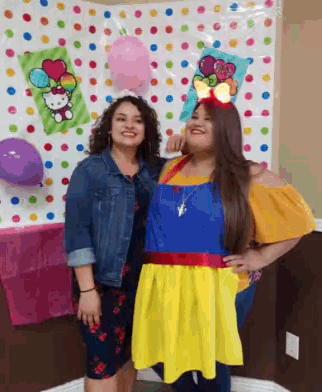two women are posing for a picture in front of a colorful polka dot wall