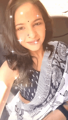 a woman with a nose ring and a black and white saree smiles for the camera