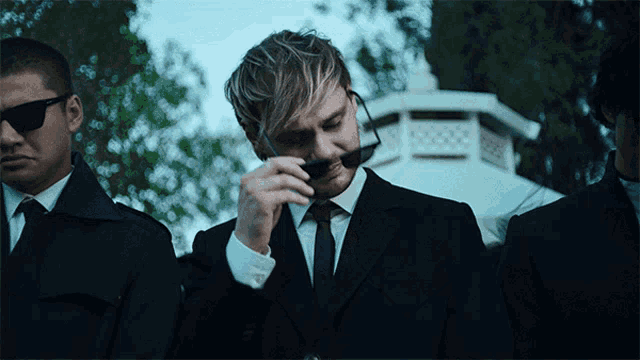 a man in a suit adjusts his sunglasses
