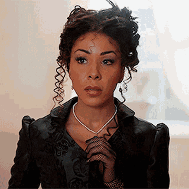 a woman with curly hair wearing a black jacket and a pearl necklace