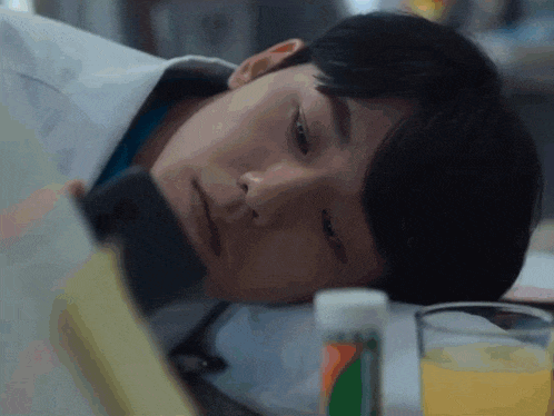 a man is laying down with a book and a glass of orange juice in front of him