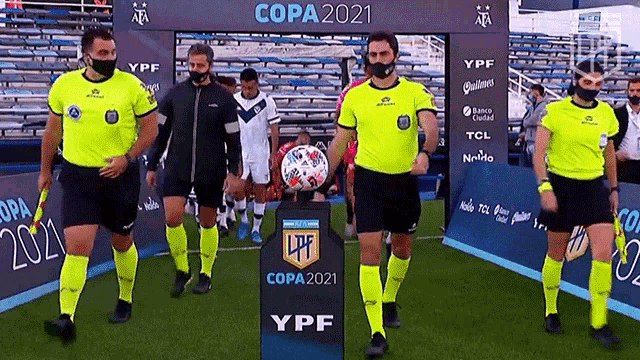 a group of referees are walking on a soccer field with a soccer ball in front of them .