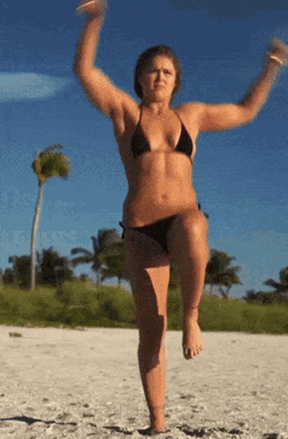 a woman in a bikini is jumping in the air on the beach