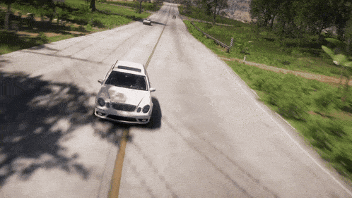 a white car is driving down a road surrounded by trees