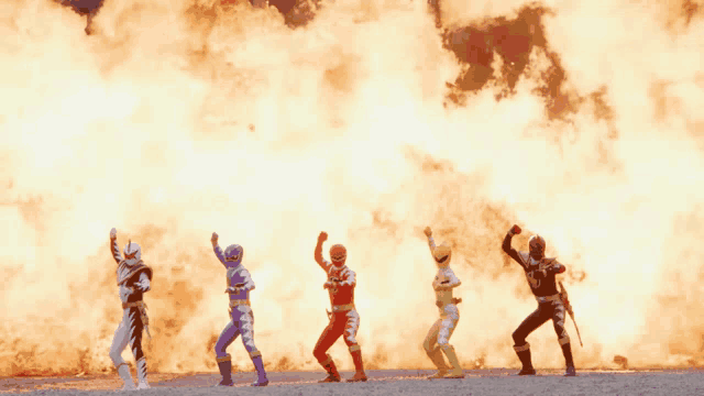 a group of power rangers are standing in front of a large fire