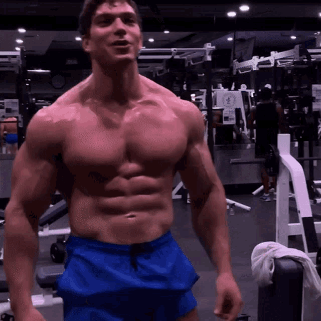 a shirtless man in blue shorts is standing in a gym looking at the camera