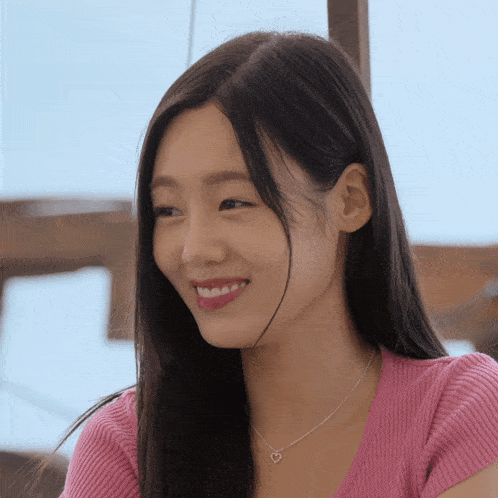 a woman wearing a pink shirt and a heart necklace smiles for the camera