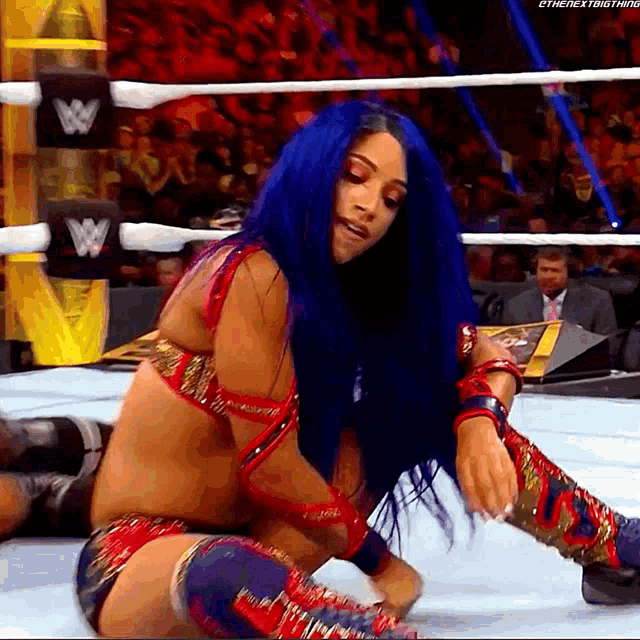a female wrestler with blue hair is kneeling down in a wrestling ring