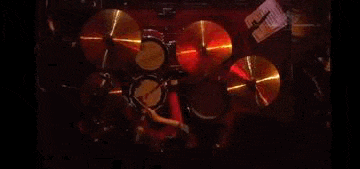 a man is playing drums on a stage in a dark room with a drum set .
