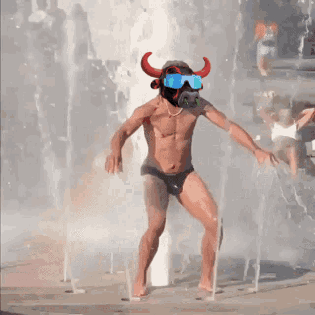 a shirtless man in a bull mask is dancing in a water fountain