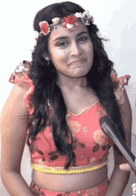 a woman wearing a flower crown is holding a microphone and making a funny face