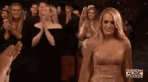 a woman in a gold dress is standing in front of a crowd of people clapping .