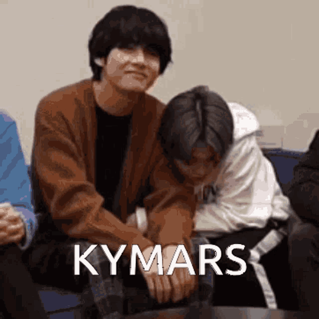 two men are sitting next to each other on a couch with the word kymars written on the bottom .