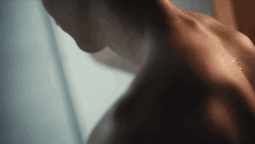 a close up of a man taking a shower with water drops on his back