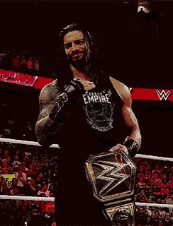 roman reigns is holding a wwe world heavyweight championship belt in a ring .