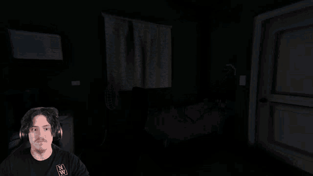 a man wearing headphones and a shirt that says nw looks at the camera in a dark room