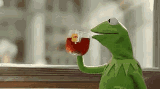 kermit the frog is drinking a glass of red tea from a cup .