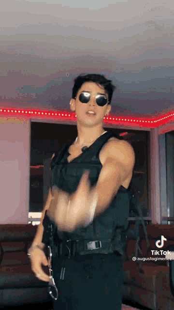 a man wearing sunglasses and a vest is dancing in a living room .