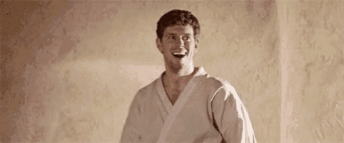 a man in a karate uniform is laughing and looking at the camera .