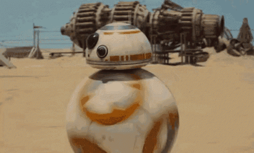 bb-8 from star wars is standing on top of a sandy beach .