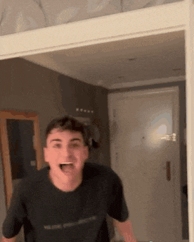 a young man in a black t-shirt is standing in a room with his mouth wide open .