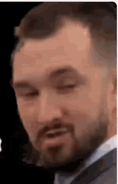 a close up of a man with a beard wearing a suit and tie .