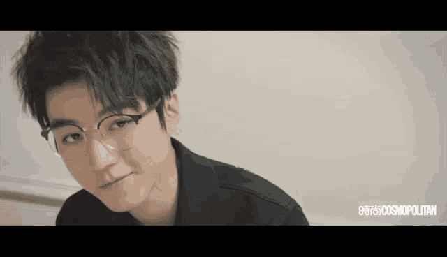 a young man wearing glasses and a black shirt looks at the camera