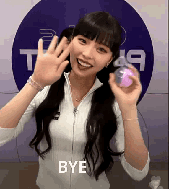 a woman holds a pink ball and says bye in front of a circle with the number 19 on it