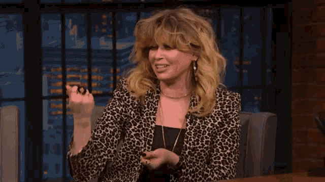a woman wearing a leopard print jacket is sitting at a table with her hands on her chest .