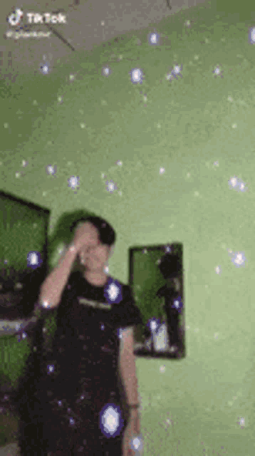 a man in a black shirt is standing in front of a green wall surrounded by bubbles .