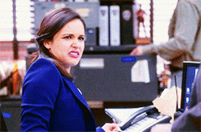 a woman in a blue jacket is sitting at a desk with a phone in her hand