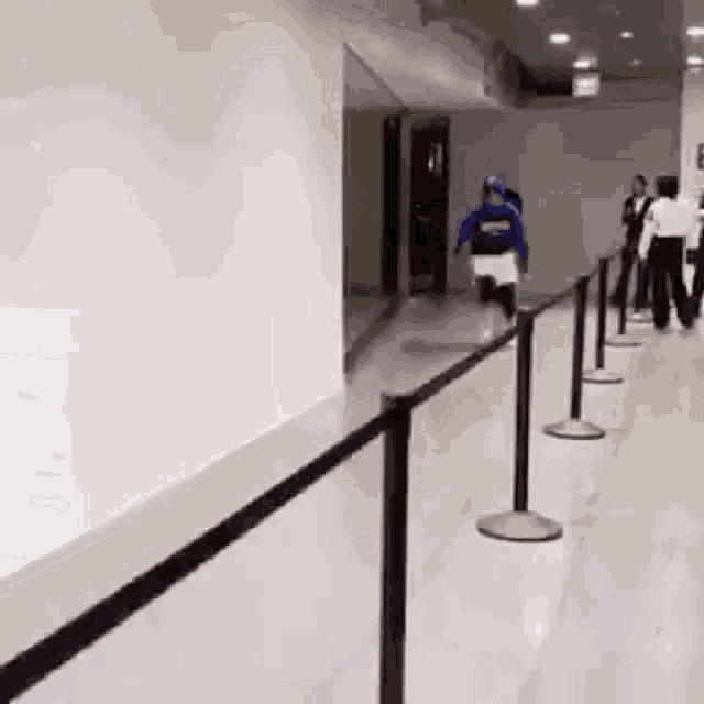 a person in a blue shirt is running down a hallway next to a black barrier .