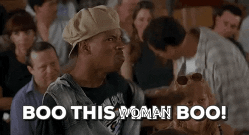 a man in a hat is standing in front of a crowd of people and says boo this woman boo .