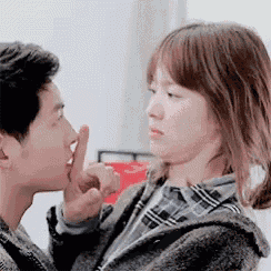 a man is kissing a woman on the cheek while she holds her finger to her lips .